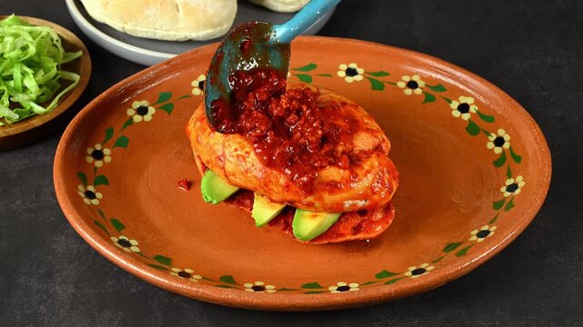 Bathing a pambazo filled with avocado, also known in Mexico as chancla poblana, in red chorizo ​​adobo