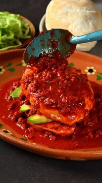 Mexican street food, bathing a pambazo filled with avocado, also known in Mexico as chancla poblana, in red chorizo ​​adobo