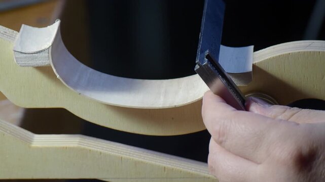 Luthier hands checking violin rib thickness on an internal mold, using a precision caliper to measure the rib curve near a block, showing accurate control during traditional violinmaking