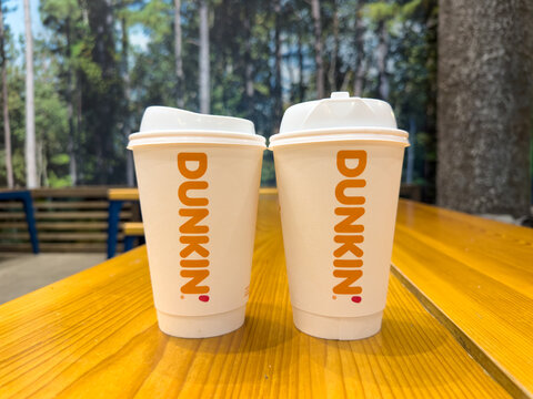 Two Dunkin Hot Coffee Cups on Wooden Table at Indoor Resort Seating