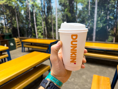 Dunkin Hot Coffee Cup Held in Hand at Indoor Lodge Seating Area