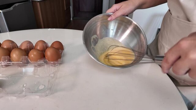 Close-up of a woman's hands beating eggs in a metal bowl on a table