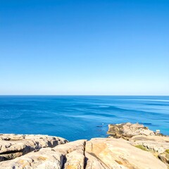 Calm ocean waters meet rugged rocky shoreline under clear blue sky