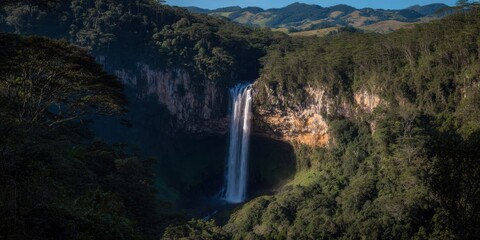 Naklejka premium Majestic Waterfall Plunging from a Rocky Cliff Into a Lush Green Rainforest Canyon, Scenic Nature Landscape for Eco Tourism Travel and Wilderness Exploration