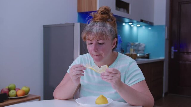 Woman eating a sour lemon while sitting at a table