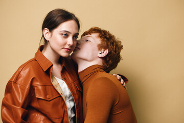 Couple with red hair and brown jacket in loving embrace against beige background. Intimate moment,...