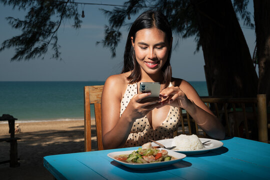 Young woman taking photo with phone while enjoying meal at seaside restaurant