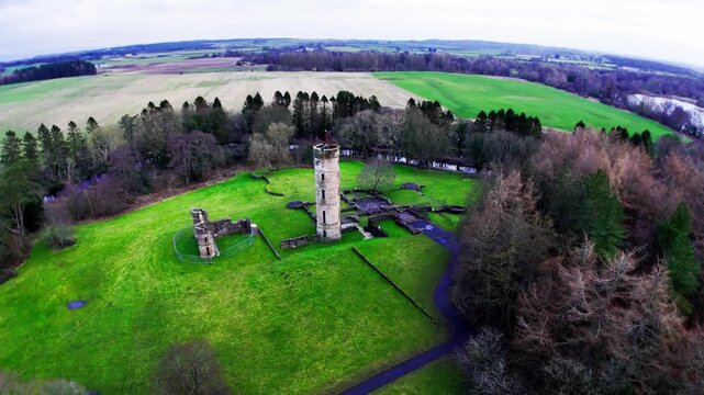 Eglinton Castle ruins in Kilwinning, Scotland, UK, circling the historic tower and stone foundations in Eglinton Country Park with surrounding woodland and fields, aerial orbital view