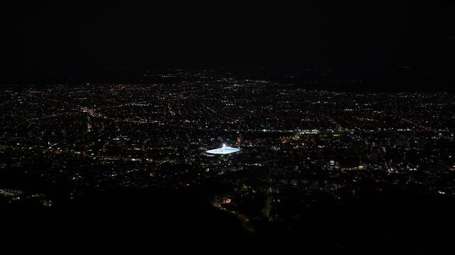 Wide panoramic night view of Cali showing illuminated buildings, urban skyline and city lights against the dark sky. The scene captures the vibrant atmosphere and metropolitan landscape of one of Colo