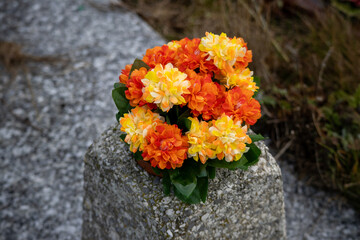 Vibrant orange and yellow artificial flower bouquet on a stone memorial pillar
