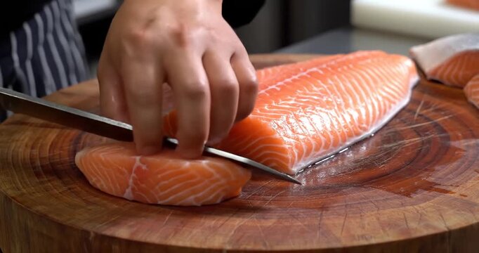 Chef skillfully slices fresh salmon fillet on a wooden cutting board in a modern kitchen