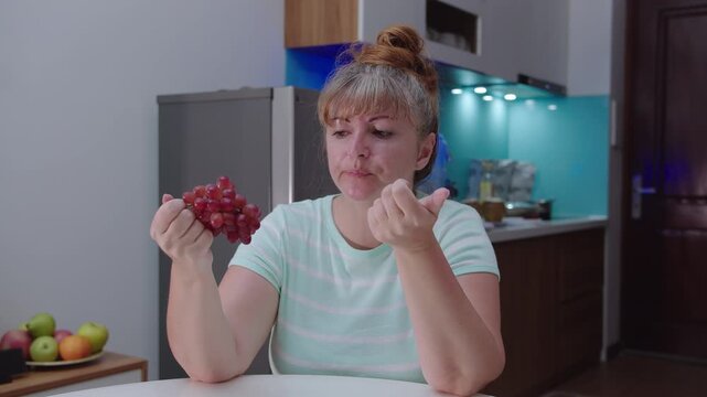 A woman eats grapes, sitting at home at the table