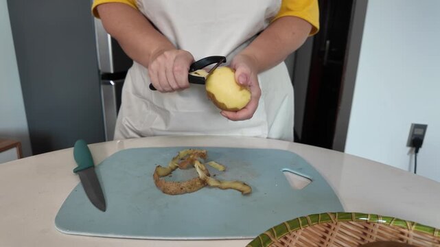 Hands of a woman who, peels potatoes with a vegetable peeler while standing at the table