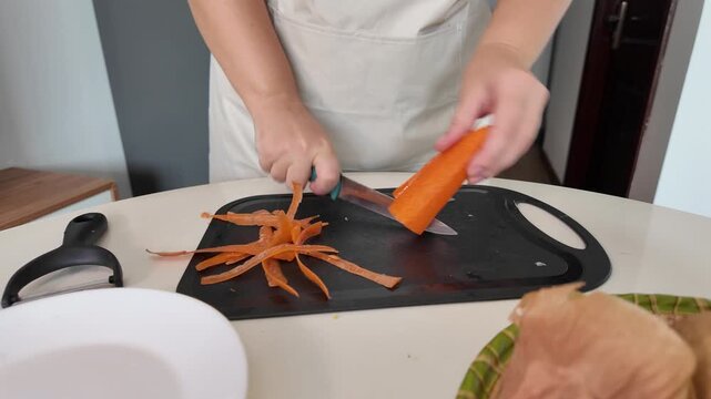 The hands of a woman standing at the kitchen table, peeling carrots with a vegetable peeler