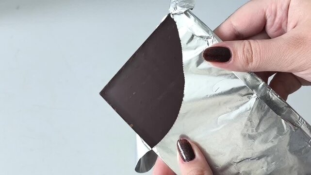 An open pack of dark chocolate. Chocolate bar in foil in a woman's hand