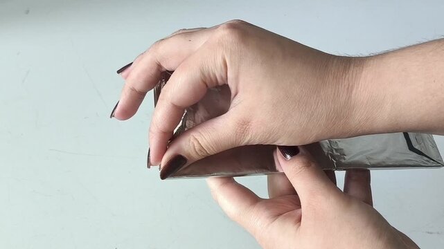 Female hands opening a package of chocolate foil. Dark chocolate in foil