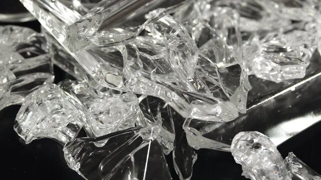 Jagged transparent glass fragments on glossy surface reflecting light with sharp edges captured in close-up hazard detail