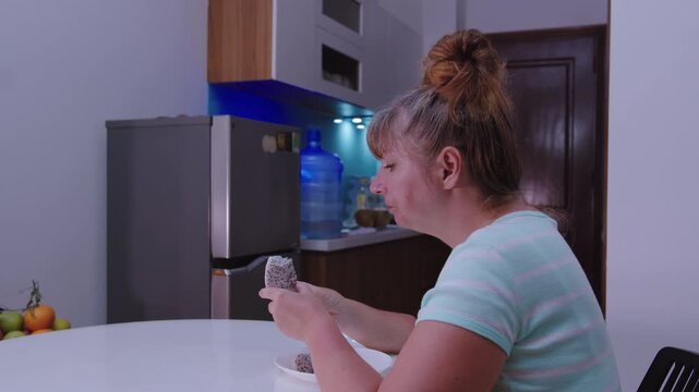 Woman sits at a table in front of the kitchen and eats a dragon fruit