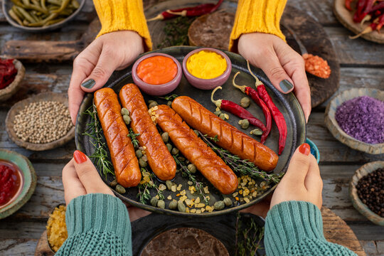 Grilled bratwurst and sausages in the plate at the hands of two women.  
