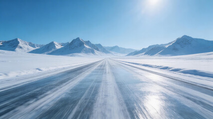 Naklejka premium Snow-covered highway stretches through arctic mountainous terrain under a bright sun. The icy road reflects sunlight, suggesting a cold, remote travel destination in a pristine winter landscape.