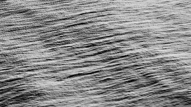 Aerial drone view of dark ocean waves forming textured ripples across the sea surface, capturing natural water motion, shifting patterns, fluid dynamics, and a calm marine atmosphere. 4K.
