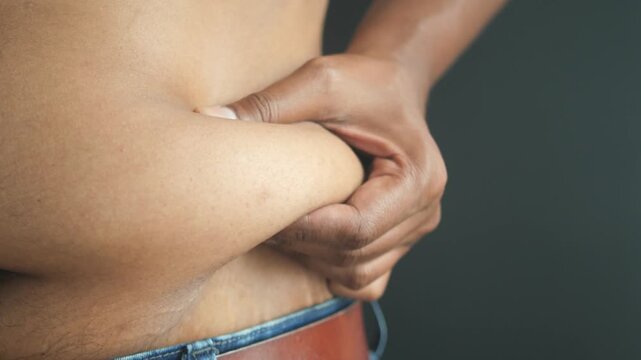 Close up shot of person pinching excess belly fat, highlighting weight gain and body concerns