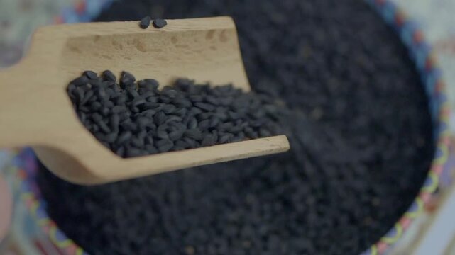 Wooden scoop filled with black cumin seeds, close-up motion revealing texture and detail