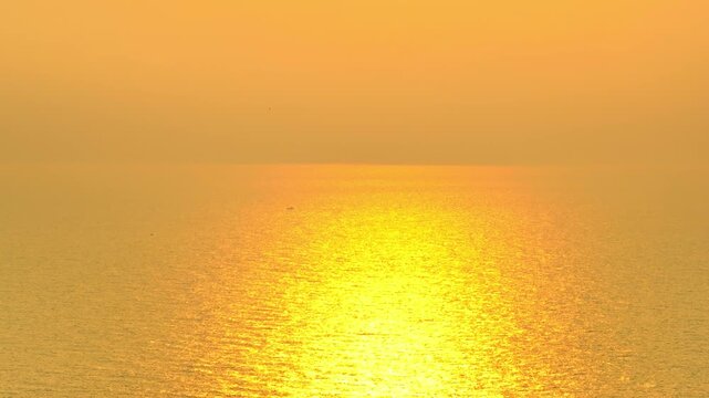 Drone shot of a glowing sunset spreading light over the ocean surface, showcasing natural beauty, gentle waves, soothing ambience, and themes of clarity, freedom, calmness, energy, connection, rhythm.