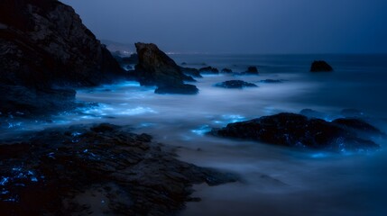 Obraz premium Magical bioluminescent waves crash on rocks serene coastal twilight scene evokes wonder