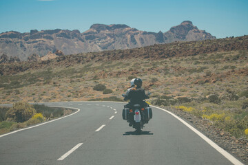 Naklejka premium Motorcycle travelers on a winding mountain road heading towards volcanic peaks with copy space