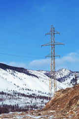 Power line stands against snowy mountains and blue sky in winter