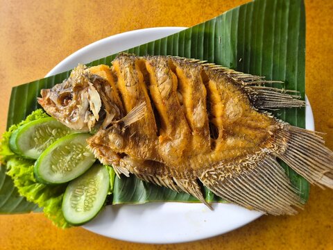 Fried gurame fish on the banana leaf with cucumber slices and lettuce,  Indonesian traditional food