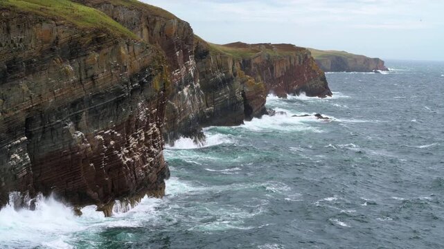 A wide shot of stormy sea and next to a cliff side beach. The waves are crushing into the rock formation and it looks magnificent. The winds are also strong. And the sky is cloudy