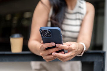 Close up of a woman looking at phone holding with both hand aside coffee standing leaning on railing