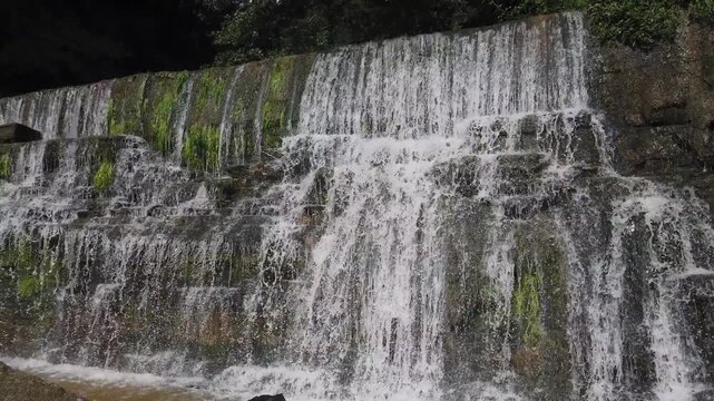 Clear water cascades over moss-covered rock layers of a scenic waterfall in Rupit, Catalonia, surrounded by lush green vegetation in a tranquil natural environment