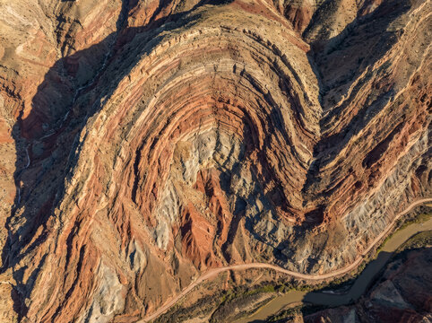 Aerial view of a massive geological fold in a desert landscape with layered rock formations and a winding river below.