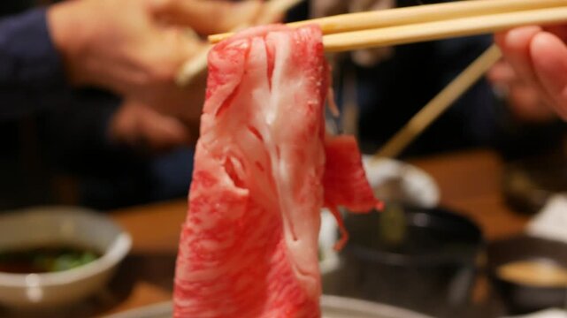 selective focusing pov to raw meat wagyu japanese A5 using chopstick pick up to boil for shabu shabu hotpot japanese food. Raw slided japanese beef for hotpot sukiyaki shabu shabu food