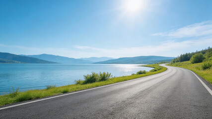 Naklejka premium A smooth, curved road runs alongside a calm lake, flanked by lush greenery. Distant mountains rise under a bright, clear sky, creating a serene, picturesque landscape ideal for travel and adventure.