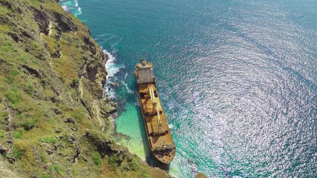 Aerial view of the abandoned MV Jernas shipwreck grounded against rocky cliffs along the coast of the Arabian Sea near Salalah, Oman.