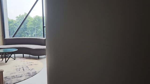 Modern luxury hotel lobby lounge with stylish curved grey sofas, elegant wooden chairs, marble floors, and large glass windows offering a bright atmosphere and scenic green outdoor views for guests