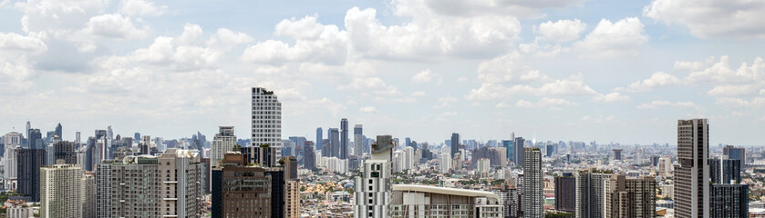 Obraz premium Expansive city skyline with dense high-rise buildings under a bright, cloudy sky, showcasing a modern urban metropolis.