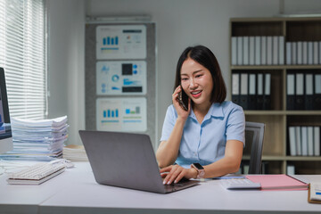 Young asian businesswoman talking on phone while working on laptop