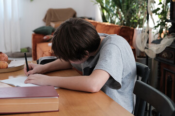 slouching, posture. A teenager does math homework, writes down examples and uses his smartphone for...