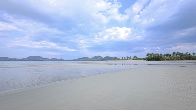 Curved shallow water edge across tidal sandflat under cloudy daylight in Thailand