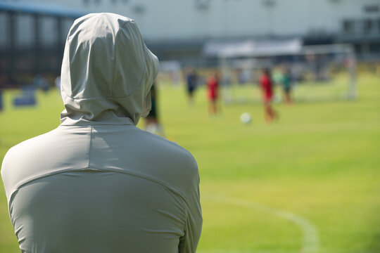 Candid back view of a supportive Asian father cheering for their son during a youth soccer match at school.
