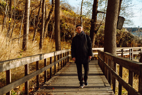 Young Man Walking on Wooden Boardwalk Through Autumn Forest