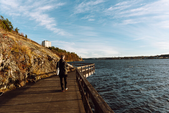 Man Walking on Wooden Pier by the Sea Under Blue Sky