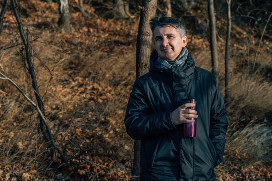 Smiling Man Holding Thermos Flask in Autumn Forest