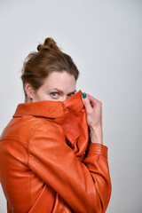 Naklejka premium Frauenportrait im Studio mit orangefarbener Lederjacke. Das Model zieht den Kragen hoch und blickt intensiv in die Kamera – modernes Fashion-Statement mit selbstbewusster Attitude.