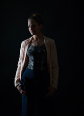 Naklejka premium Low-Key-Portrait eines Models im Mantel vor dunklem Hintergrund. Dramatisches Licht, starke Schatten und roter Lippenstift setzen elegante, ausdrucksstarke Akzente.